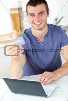 Charismatic young man holding a card using his laptop in the kit