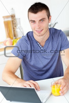Charming young man using his laptop holding orange juice in the 