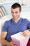 Laughing caucasian man eating popcorn on a sofa