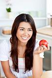 Radiant asian woman holding an apple in the kitchen 