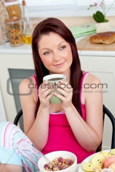 Cute woman eating her breakfast at home holding a cup of coffee
