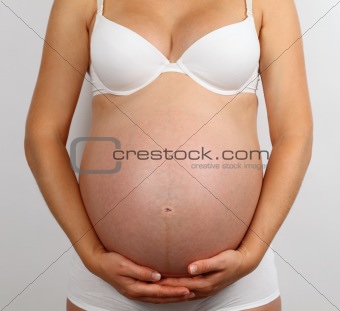 Young pregnant woman in white underwear holding her belly