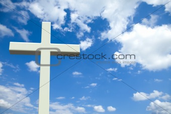 White Christian cross in front of a cloudy sky with copyspace