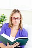 Concentrated young woman wearing red glasses reading a book on a