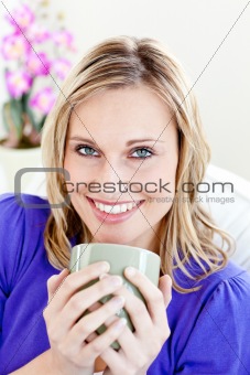 Joyful young woman holding a cup of coffee on a sofa