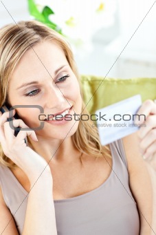 Beautiful young woman holding a card and phoning lying a sofa