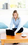 Glowing businesswoman using her laptop sitting on a sofa
