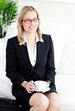 Delighted businesswoman wearing glasses drinking coffee sitting 