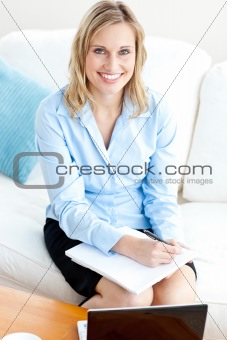 Radiant businesswoman writing in her notepad and using her lapto