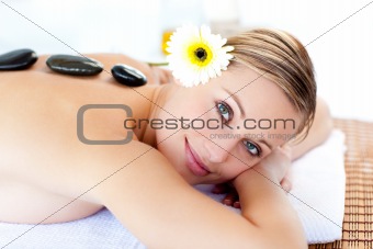 Glowing young woman with hot stones on her back smiling at the c