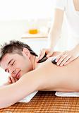 Happy young man enjoying a back massage with hot stone