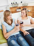 Charming two women drinking wine sitting on a sofa