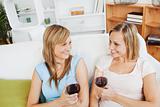Happy two women drinking wine sitting on a sofa 
