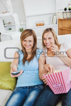 Joyful female friends watching television and eating popcorn 