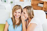 Portrait of two caucasian female friends telling secrets at home