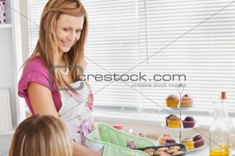 Positive young woman baking cookies for her girlfriend 