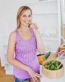 Smiling woman eating cucumber in the kitchen