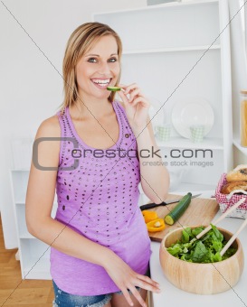 Smiling woman eating cucumber in the kitchen