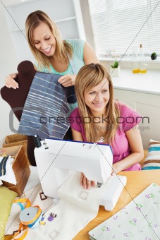 Happy young female friends sewing clothes together at home