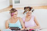 Close female friends with hair rollers eating chocolate reading 