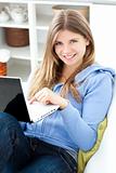 Positive woman using a laptop sitting on a sofa