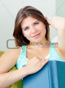 Bright caucasian woman holding a book sitting on a sofa