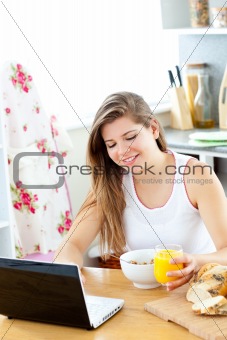 Enthusiastic young woman using her laptop while having breakfast