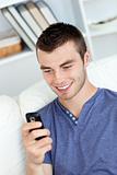Charming young man sending a text and smiling in the living-room