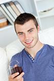 Charismatic young man holding a glass of wine sitting on a sofa 
