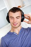 Relaxed young man listening to music with headphones in the livi
