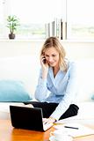 Busy businesswoman using her phone and laptop in her living-room at home