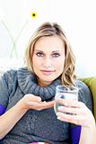 sick woman holding pills and a glass of water sitting in her sofa