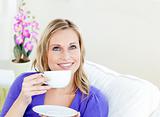 Bright woman enjoying her coffee sitting on a sofa in the living