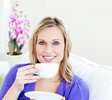 Charming woman enjoying her coffee sitting on a sofa in the livi