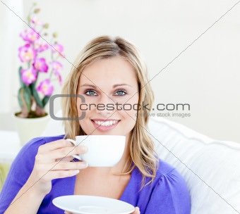 Charming woman enjoying her coffee sitting on a sofa in the livi