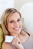radiant woman holding a credit card lying in the sofa