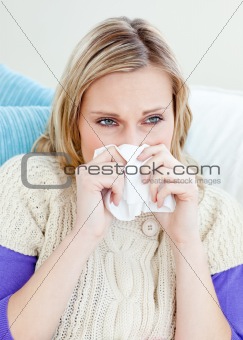 sick woman using a tissue sitting on a sofa at home