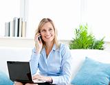 Smiling businesswoman talking on phone and using her laptop sitt