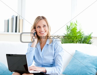 Smiling businesswoman talking on phone and using her laptop sitt