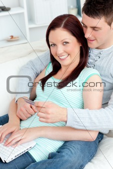 Loving couple using a laptop and holding a credit card to buy on