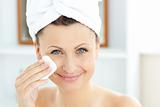 Joyful young woman with a towel putting cream on her face in the