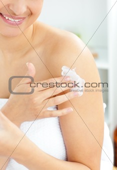 Happy young woman with a towel putting cream on her face in the 