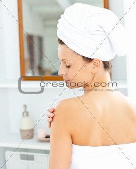 Pleased young woman with a towel putting cream on her face in th