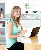 Delighted blond woman using her laptop smiling at the camera at 