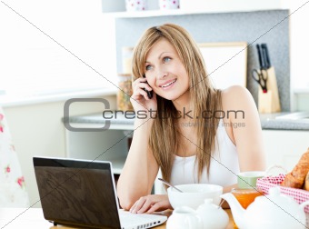 Young caucasian woman using her laptop and talking on phone duri