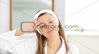 Positive woman putting cream on her face wearing a headband in t
