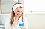 Radiant woman putting cream on her face wearing a headband in th