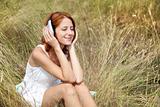 Beautiful red-haired girl at grass with headphones