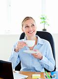 Delighted businesswoman drinking coffee in front of her laptop i