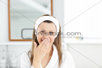 Tired young woman yawning in the bathroom looking at the camera 